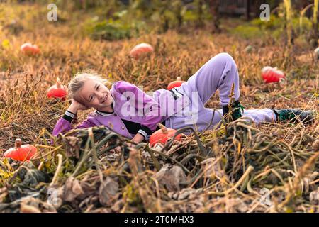 La ragazza tiene in mano una grande zucca d'arancio fresca, raccolta nell'orto. bambino al tramonto con verdure in mano. stagione del raccolto. Cibo sano. Li Foto Stock