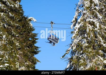 Operazione di seggiovia nella Foresta Nera. Gondola blu tra abeti verdi con neve. Trasporto in funivia per sciatori e snowboard. Germania, Feldberg Foto Stock