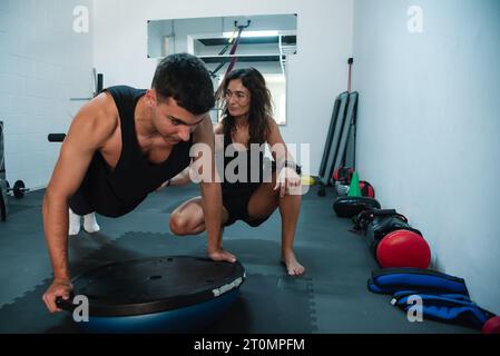 Il personal trainer assiste e dirige un giovane durante la sua sessione di allenamento in palestra. L'istruttore, un esperto di fitness, fornisce istruzioni precise Foto Stock