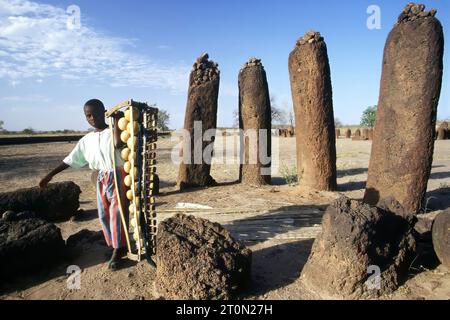 Un ragazzo porta con sé un tradizionale strumento di musica balafon presso i circoli di pietra di Wassu, sito patrimonio dell'umanità dell'UNESCO, il Gambia, Africa Foto Stock