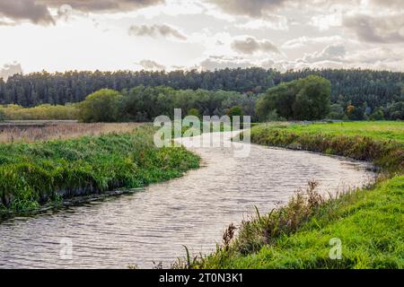 Splendida vista del paesaggio autunnale con lo stretto fiume che scorre tra campi agricoli sullo sfondo del tramonto. Foto Stock