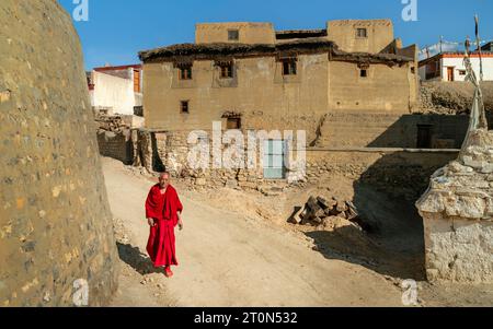 Il monaco buddista in abiti tradizionali cammina lungo una strada sterrata fiancheggiata da case nel villaggio di Kibber, Himachal Pradesh, India. Foto Stock