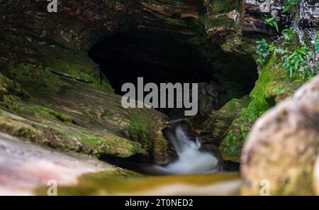 Grotta scura con cascata di setosa che abbraccia la luce del sole, circondata dalla natura Foto Stock