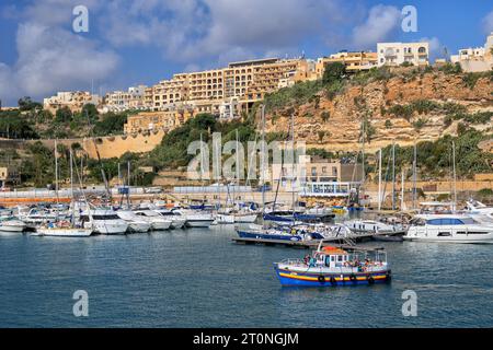 Mgarr, Gozo, Malta - 15 ottobre 2019: Città e porto di Mgarr sull'isola di Gozo, yacht e barche a vela nel porticciolo e condomini su una scogliera. Foto Stock