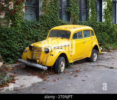 Auto retrò gialla brillante in piedi vicino alla casa. Vecchia macchina arrugginita. Foto Stock