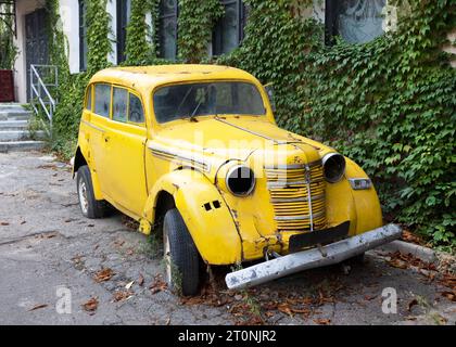 Un'auto retrò di colore giallo brillante si trova nel cortile della casa. Vecchia macchina Rusty. Foto Stock