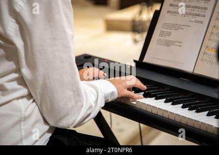 Dettaglio delle mani di un uomo caucasico in abbigliamento classico che suona musica su una tastiera in un ambiente interno della chiesa. Foto Stock