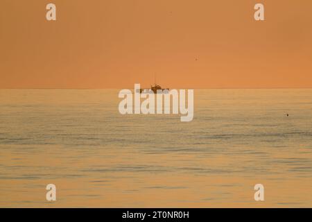 Un peschereccio al largo è avvolto da raggi scagliati da un'alba del Massachusetts di prima mattina. Foto Stock
