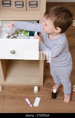 Il bambino del bambino ha aperto il cassetto dell'armadietto con le pillole e la medicina. Bambino che tiene una confezione di pillole nel salotto di casa. Bambino di età un anno nove mese Foto Stock