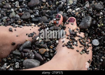 I piedi della donna sepolti in ciottoli su una spiaggia Foto Stock