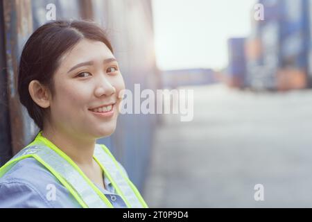 La donna asiatica lavoratrice di banchina felice controlla il carico dei container nei cantieri navali. Dipendente responsabile del personale marittimo e di trasporto. carico di carico per la spedizione da parte dell'operatore Foto Stock