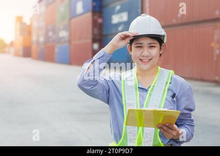 La donna asiatica lavoratrice di banchina felice controlla il carico dei container nei cantieri navali. Dipendente responsabile del personale marittimo e di trasporto. carico di carico per la spedizione da parte dell'operatore Foto Stock