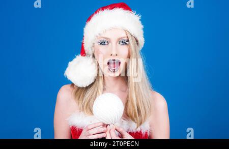 Buon Natale e felice anno nuovo. Carina ragazza con il cappello di Babbo Natale con la palla di Natale. Vacanze invernali, Natale e Capodanno. Babbo Natale con brillante Foto Stock