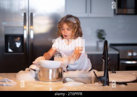 Simpatici ragazzi gemelli che aiutano in cucina con il lavaggio dei piatti. I bambini si divertono con i lavori di casa. Piccola domestica. Piatti per il lavaggio e la pulizia dei bambini nel kit Foto Stock