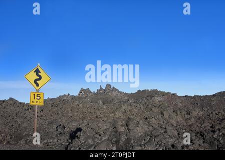 Un segnale stradale giallo avverte delle curve davanti al passo McKenzie, nell'Oregon centrale. Il campo di lava sorge oltre la strada. Foto Stock