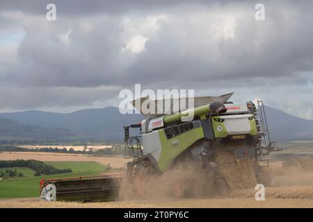 Una mietitrebbia Claas Lexion vista da dietro in Clouds of Debris che lavora in un Hillside Field of Barley con vista sull'Aberdeenshire Foto Stock
