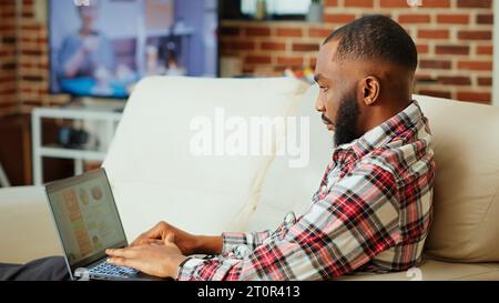 Dipendente remoto che utilizza grafici di dati statistici di analisi online per identificare le tendenze e prevedere i risultati aziendali. mentre lavorate da casa. Telelavoratore che monitora gli indicatori chiave delle prestazioni del mercato Foto Stock