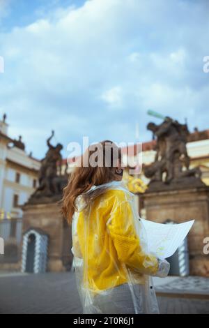 Vista da dietro donna turistica in camicetta gialla e impermeabile a Praga Repubblica Ceca con mappa vicino al Castello di Praga. Foto Stock