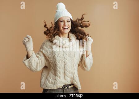Ciao inverno. donna felice ed elegante con maglione beige, guanti e cappello isolati sul salto di fondo beige. Foto Stock