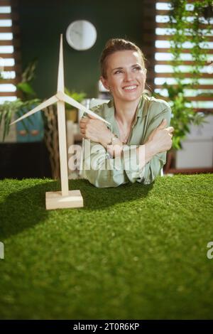 Trend ecologici. penosa e moderna proprietaria di una piccola impresa con camicetta verde in un moderno ufficio verde con mulino a vento Foto Stock