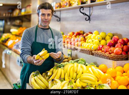 Uomo adulto che vende mazzi di banane in negozio Foto Stock