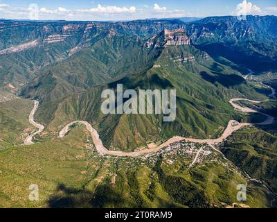 Dall'occhio di un drone, il panorama aereo dell'Urique Canyon all'interno del Copper Canyon, Chihuahua svela una strada tortuosa che conduce al villaggio annidato di Uriq Foto Stock