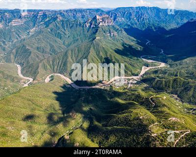 Dall'occhio di un drone, il panorama aereo dell'Urique Canyon all'interno del Copper Canyon, Chihuahua svela una strada tortuosa che conduce al villaggio annidato di Uriq Foto Stock