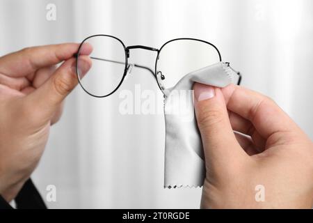 Uomo che pulisce gli occhiali con un panno in microfibra per interni, primo piano Foto Stock