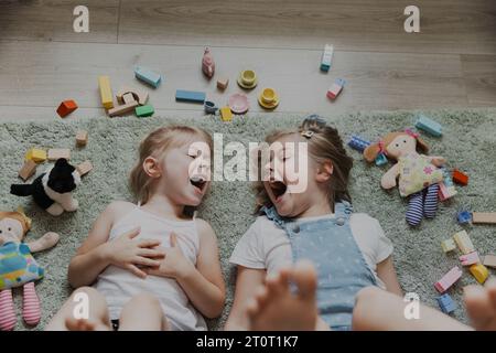 Vista dall'alto dei bambini che giocano con giocattoli colorati. Ritratto di bambini sdraiati sul tappeto nella camera da letto o nell'asilo. Due sorelle sorridenti felici. Giochi educativi ecologici Foto Stock