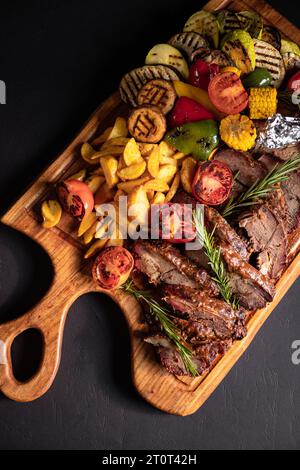 pezzi di bistecca fritti con verdure sulla griglia su un vassoio di legno Foto Stock