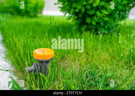 Primo piano di un irrigatore multifunzionale regolabile per prati. Irroratrice per erba arancione con diverse modalità. Irrigazione settoriale inserita nel terreno nel ga Foto Stock