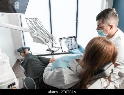 Il paziente riceve cure dentistiche e consigli da uno specialista esperto presso il centro medico. Stomatolo esamina e analizza una radiografia della bocca Foto Stock