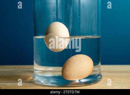 Confronto con uova fresche commestibili e vecchie marciume. L'uovo di gallina fresco commestibile è incassato sul fondo del vaso di vetro e l'uovo cattivo marcio sta galleggiando. Foto Stock