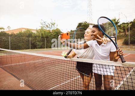 Ritratto di due giovani belle donne con vestiti da tennis e racchette in un campo da tennis pronto a giocare. Foto Stock