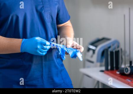 Un medico maschio indossa guanti blu prima di iniziare una procedura. Foto Stock