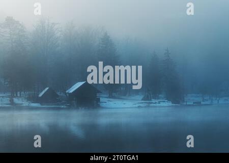 Bohinj Lake Boathouse sul lungomare nella nebbiosa mattinata invernale con cabine e moli in legno, attenzione selettiva Foto Stock