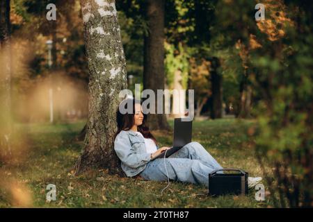 Una donna in natura lavora con un laptop caricando da una stazione di ricarica portatile Foto Stock
