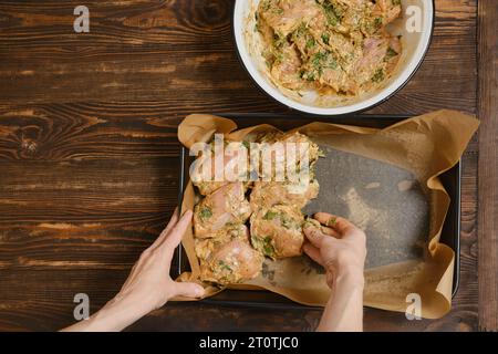 Mani di una donna che mette le cosce di pollo nel vassoio da forno di una ciotola Foto Stock