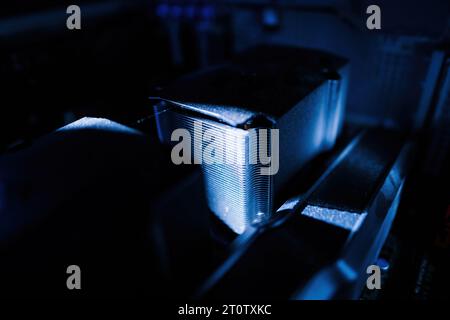 Un cast di colore blu illumina un primo piano di un nuovo e potente raffreddatore per computer CPU polveroso, con un fascio luminoso che accentua l'intricata griglia del radiatore Foto Stock