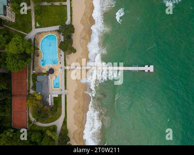 Vista aerea dall'alto di un lungo molo che si estende fino al mare, situata sul fronte spiaggia di un hotel, perfetta per passeggiate romantiche e pittoresche vedute dell'oceano. Foto Stock