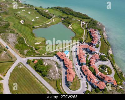 La vista aerea del campo da golf si estende sotto, con i suoi lussureggianti fairway verdi che completano il panorama mozzafiato della costa. Tra i pittoreschi l Foto Stock