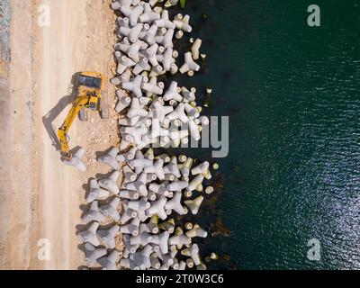 Un escavatore costruisce diligentemente un molo o un frangiflutti nel mare, il suo potente braccio che si estende dalla riva, creando una struttura resiliente in mezzo Foto Stock
