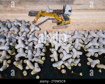 Un escavatore costruisce diligentemente un molo o un frangiflutti nel mare, il suo potente braccio che si estende dalla riva, creando una struttura resiliente in mezzo Foto Stock