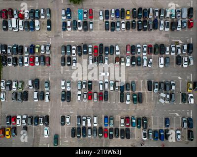 La vista aerea dei droni rivela un parcheggio densamente affollato pieno di auto. I punti colorati formano un motivo che riflette il trambusto della vita urbana. Foto Stock