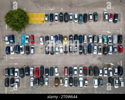 La vista aerea dei droni rivela un parcheggio densamente affollato pieno di auto. I punti colorati formano un motivo che riflette il trambusto della vita urbana. Foto Stock