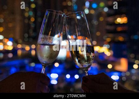 Due persone che brindano con un bicchiere di champagne davanti alla vista della città di notte Foto Stock