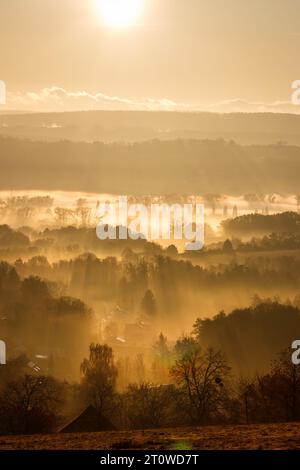 Nebbia autunnale con raggi del sole sulla campagna durante l'alba. Paesaggio autunnale dall'alto. Freddo mattutino Foto Stock