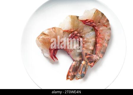 Tre grandi gamberi tigre crudi senza testa e puliti per cucinare su un piatto bianco, vista dall'alto, spazio di copia, messa a fuoco selezionata Foto Stock