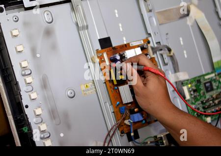 Cairo, Egitto, 3 ottobre 2023: Ingegnere tecnico che utilizza un multimetro digitale, circuito di alimentazione della scheda principale TV LCD, fili, trasformatori, resis Foto Stock