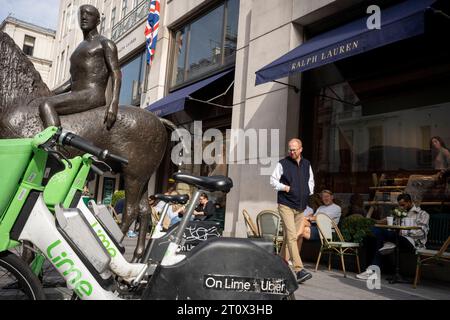 La scultura intitolata Horse and Rider si erge sopra una collezione di eBike a noleggio Lime in Bond Street, il 9 ottobre 2023, a Londra, in Inghilterra. "Cavallo e cavaliere" è una scultura equestre in bronzo del 1974 di Elisabeth Frink. Il lavoro è stato commissionato per un sito a Mayfair; un altro cast è a Winchester. È stato descritto da Frink come "un simbolo senza età dell'uomo e del cavallo". Foto Stock